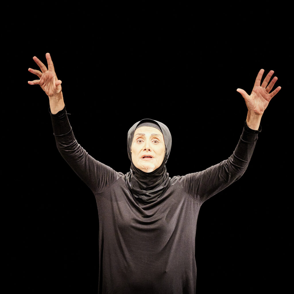 La comédienne Hanane Hajj Ali vêtue de noir et les bras tendus vers le ciel, dans le spectacle "Jogging" au Théâtre Silvia-Monfort